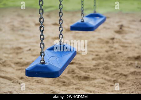 Zwei leere blaue Plastikschaukeln für Kinder hängen an Metallketten auf einem Spielplatz während der Abriegelung in der Coronavirus-Pandemi Stockfoto