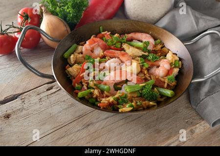 Spanische Paella, Reisgericht mit Garnelen, Huhn und Gemüse in einer flachen Pfanne auf einem rustikalen Holztisch, Kopierraum, ausgewählter Fokus Stockfoto