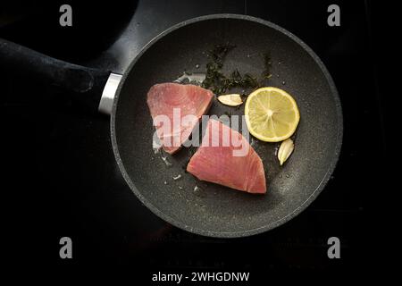 Frische, rohe Thunfischsteaks mit Zitrone, Knoblauch und Thymiankraut in einer Pfanne auf einem Backofen, Kopierraum, Blick aus einem hohen Winkel von der direkten Stockfoto