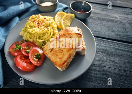 Gesunde Low Carb Diät Mahlzeit mit frittierten Thunfischsteaks, wirsingkohl, Tomaten und Zitrone auf einer blauen Platte und einem dunkelblauen rustikalen Holz Stockfoto