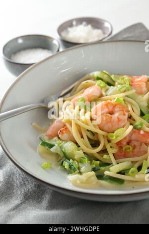 Spaghetti, Garnelen, Zucchini und Frühlingszwiebeln, eine gesunde mediterrane Mahlzeit auf einem grauen Teller mit Gabel, Serviette und Gewürzschleife Stockfoto