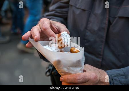 Hände eines Mannes mit einer Papiertüte Mutzenmandeln, frittiertes süßes Gebäck mit Mandeln bedeckt mit Puderzucker, traditionell Stockfoto