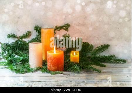 Zweiter Adventsstil, Anordnung mit vier Kerzen in Orange und Gelb, zwei mit Flamme, Tannenzweige auf hellem rustikalem Holz, Stockfoto