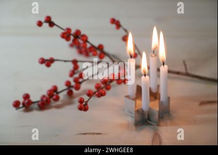 Mini-Adventskranz, vier kleine Kerzen auf einem Ausstecher in Sternform vor einem stechpalmenzweig mit roten Beeren auf einem Holz Stockfoto