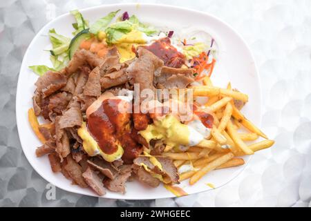 Döner Kebab auf einem Teller mit Pommes frites, Salat und verschiedenen Saucen, beliebtes Fast Food aus der türkischen Küche, Kopierraum, High ang Stockfoto