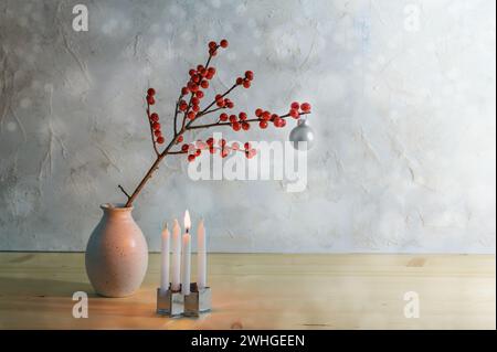 Minimalistischer erster Advent mit vier kleinen Kerzen, einer brennt und einem Beerenzweig mit einer silbernen weihnachtskugel in einer Vase, verschneit Stockfoto