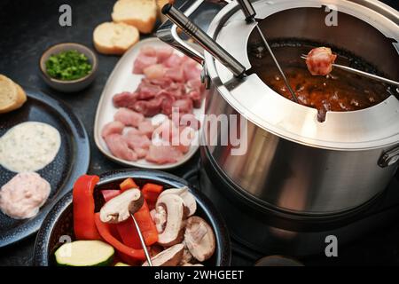 Deutsches Fondue mit rohem Fleisch und Gemüse, das auf langen Gabeln in einem Topf mit kochendem Öl frittiert wird, oft für Familie und Pommes frites serviert Stockfoto