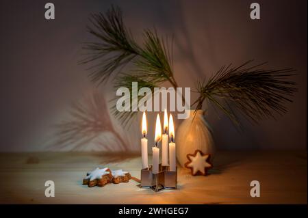 Kleine Adventskerzen auf einem Ausstecher, Zimt-Sternkekse, ein Kiefernzweig in einer Vase auf einem Holztisch, winzige Dekoration Stockfoto