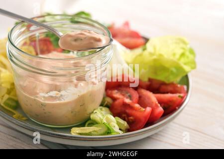 Salatdressing von Skyr auf einem Löffel und in einem Glas auf einem Teller mit Salatscheiben und Tomaten, gesunde Rohkost Mahlzeit Stockfoto