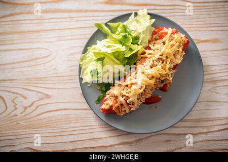 Spitz rote Paprika gebacken mit Reis, Thunfisch und Käse, Salatsalat mit Petersilie auf grauem blauem Teller, rustikales Holz Stockfoto