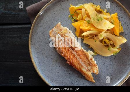 Kabeljau mit Fenchelgemüse und Orangenscheiben auf blauem Teller und dunklem Tisch, Hochwinkel von oben Stockfoto