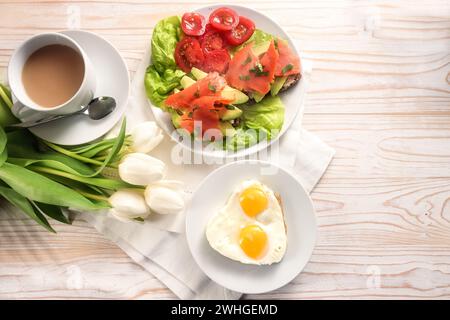 Gesundes Frühstück mit Liebe zubereitet, Spiegeleier in Herzform, Sandwich mit Avocado und Räucherlachs auf Salat und Tomaten Stockfoto