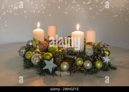 Zweiter Adventskranz mit zwei brennenden weißen Kerzen und grüner Weihnachtsdekoration auf einem Tisch, Wohnkultur für den ersten Sonntag, Stockfoto