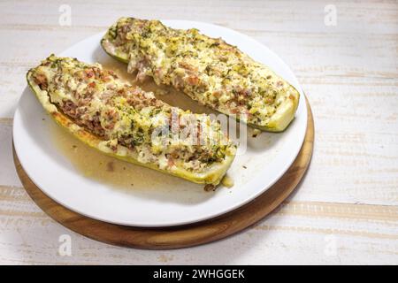 Gebackene Zucchini- oder Zucchini-Boote gefüllt mit Hackfleisch, Zwiebeln und Sahne frisch aus dem Ofen auf einem weißen Teller und einem LIG Stockfoto