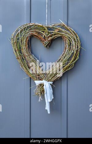 Trockene Zweige in Herzform, die an einer blauen grauen Holztür hängen, Willkommenssymbol für Freundlichkeit und Liebe, hausgemachte Dekoration für Stockfoto