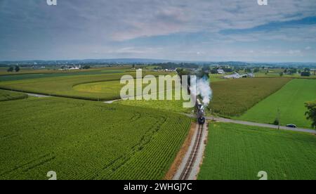 Drohne Blick auf eine antike Dampfmaschine, Annäherung, Dampfblasen und Reisen entlang der Landschaft an einem sonnigen Tag Stockfoto