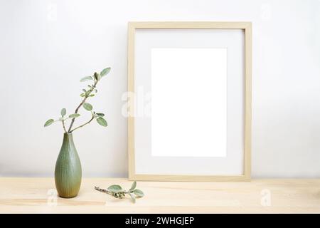 Leerer hölzerner Bilderrahmen mit Passepartout als Modell und einer Vase mit Salbeizweig auf einem Leuchttisch oder Schreibtisch vor einem weißen Stockfoto