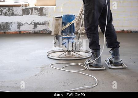 Stampfen und Schleifen von halbtrockenen Estrichen mit einer Maschine mit einer rotierenden Scheibe zum Nivellieren. Bau eines Betonbodens i Stockfoto