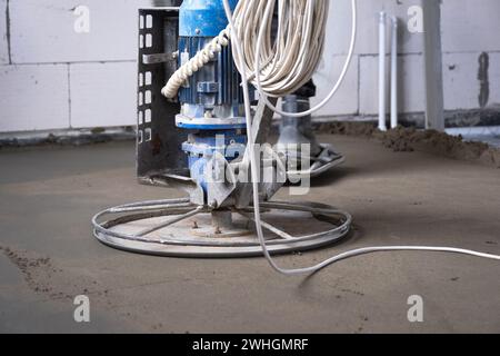 Stampfen und Schleifen von halbtrockenen Estrichen mit einer Maschine mit einer rotierenden Scheibe zum Nivellieren. Bau eines Betonbodens i Stockfoto