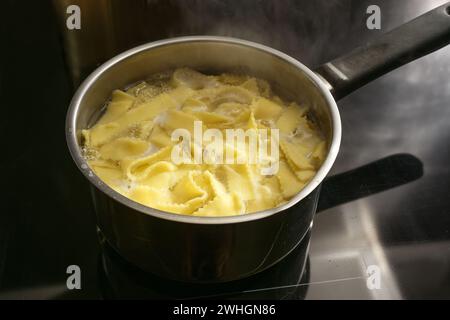 Nudelnudeln werden in kochendem Wasser in einem Topf auf einem schwarzen Herd gekocht, Lebensmittelkonzept, Kopierraum, ausgewählter Fokus Stockfoto