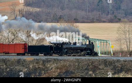 Blick auf einen restaurierten Dampfzug mit Schmalspur, der Rauch bläst und durch das Ackerland fährt Stockfoto