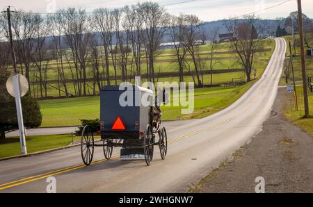 Blick auf ein Amish-Pferd und Buggy, das an einem Dezembertag auf einer Landstraße einen Hügel hinunter fährt Stockfoto