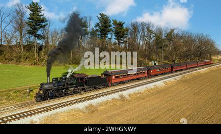 Drohnenansicht eines restaurierten Dampfzuges, der durch Farmland fährt und bis zur kleinen Station fährt Stockfoto