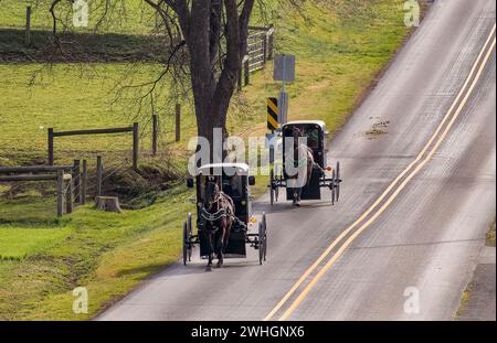 Blick auf zwei Amish Horse und Buggies, die auf einer Landstraße durch Farmland fahren Stockfoto