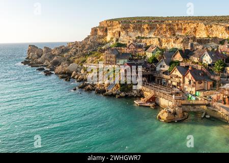 Malta, Il-Mellieha. Blick auf das berühmte Popeye Village in Anchor Bay. Türkisfarbenes Meer, blauer Himmel und Sonnenuntergang auf den Klippen Stockfoto