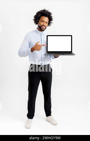 Lächelnder afroamerikanischer Geschäftsmann in formeller Kleidung zeigt Laptop mit leerem Display isoliert auf weiß. Männlicher Mitarbeiter zeigt mit dem Finger auf den leeren Bildschirm, Werbung für neue App, Präsentation von Neuheit Stockfoto