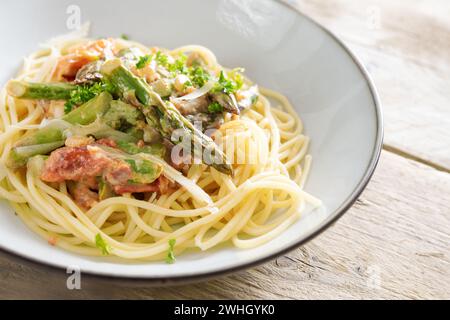 Grüner Spargel in Tomatensauce auf Spaghetti mit Parmesan und Petersilie garnieren auf einem hellgrauen Teller auf einem rustikalen Holztisch, c Stockfoto