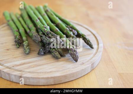 Frischer grüner Spargel auf einem Schneidebrett und einem Holztisch, köstliches Frühlingsgemüse, Kopierraum, ausgewählter Fokus Stockfoto