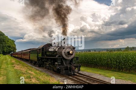 Frontalansicht des antiken Passagierzuges, der sich nähert und Schwarzen Rauch mit herannahenden Sturmwolken bläst Stockfoto