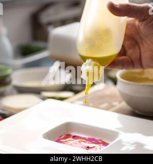 Gourmetkoch tropft kostbares Öl aus einer Flasche in eine Rote-Bete-Sauce, um ein Menü auf einem weißen Teller zu bereiten, kreative Kekse Stockfoto