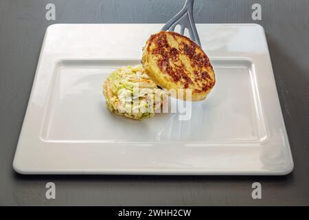 Der Fladenbrotknödel wird auf rundes Gemüse aus Karotten und Spitzkohl auf einem modernen weißen Teller, köstliches Gemüse, gelegt Stockfoto