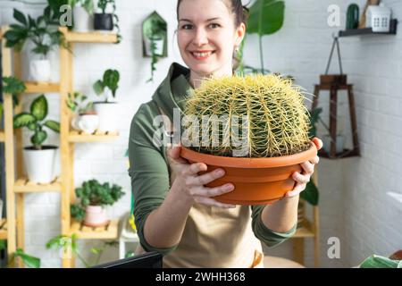 Großer echinocactus Gruzoni in den Händen einer Frau im Inneren eines Gewächshauses mit Regalsammlungen von Hauspflanzen Stockfoto