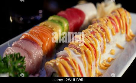 Verschiedene Sushi-Brötchen auf weißem Teller mit goldener Sauce Stockfoto