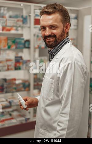 Männlicher Apotheker und weißes Fell, das Nasenspray während der Arbeit in einer Apotheke hält Stockfoto