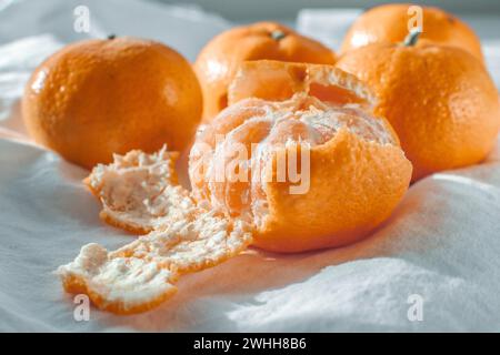 Mehrere reife orangene Mandarinen auf einer weißen Baumwolltischdecke mit ungleichmäßigem Schatten Stockfoto