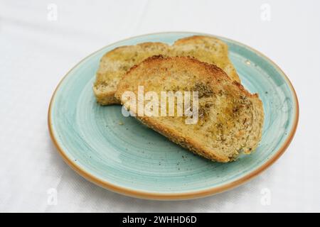 Geröstetes Brot mit Olivenöl, Kräutern und Knoblauchsalz auf blauer Platte, Kopierraum, ausgewählter Fokus, geringe Schärfentiefe Stockfoto