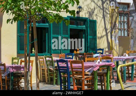 Rustikale mediterrane Taverne oder zwangloses Straßenrestaurant mit verschiedenen bemalten Holzstühlen an den Tischen vor dem Windo Stockfoto
