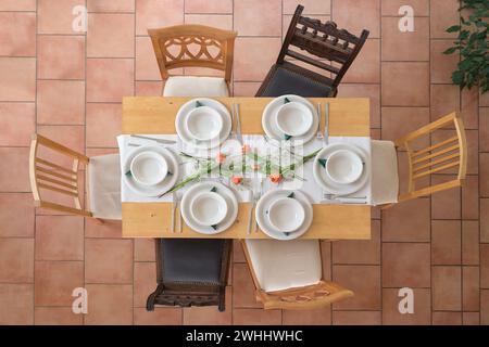 Holztisch mit sechs leeren weißen Tellern und Schüsseln, Besteck und Tulpenblumen, verschiedene Vintage-Stühle auf einem Stockfoto