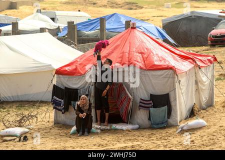 Rafah, Gaza. Februar 2024. Vertriebene Palästinenser sitzen vor einem provisorischen Zelt, während palästinensische Familien in der Mawasi-Region Zuflucht suchen, während sie sich bemühen, sauberes Wasser, Nahrung und Medikamente zu finden, während die israelischen Angriffe am Samstag, den 10. Februar 2024, in Rafah, Gaza, fortgesetzt werden. Foto: Ismael Mohamad/UPI Credit: UPI/Alamy Live News Stockfoto