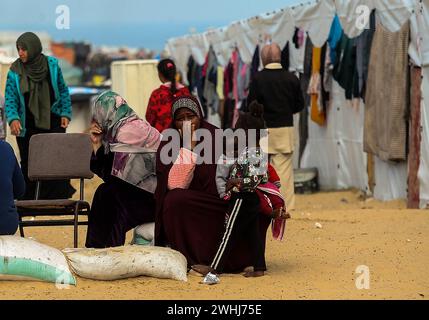 Rafah, Gaza. Februar 2024. Vertriebene Palästinenser sitzen vor einem provisorischen Zelt, während palästinensische Familien in der Mawasi-Region Zuflucht suchen, während sie sich bemühen, sauberes Wasser, Nahrung und Medikamente zu finden, während die israelischen Angriffe am Samstag, den 10. Februar 2024, in Rafah, Gaza, fortgesetzt werden. Foto: Ismael Mohamad/UPI Credit: UPI/Alamy Live News Stockfoto