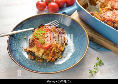 Lasagne-Portion auf einer blauen Platte, Auflaufform mit Nudelschichten, Bolognese-Sauce, Hackfleisch, Gemüse und Tomaten, belegt Stockfoto