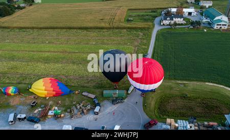 Drohnenansicht mehrerer farbenfroher Heißluftballons, die auf Bauernhöfen, Feldern und Häusern landen Stockfoto