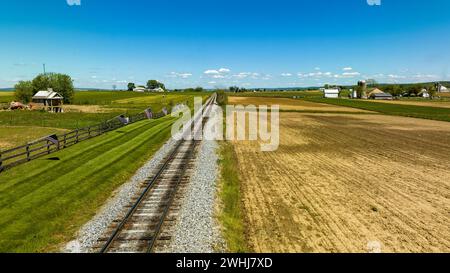 Aus der Vogelperspektive eines Single Rail Road Track, der durch Farmland mit einem Zaun mit amerikanischer Flagge führt Stockfoto