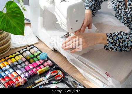 Frau Hand Nahaufnahme näht Tüll auf elektrische Nähmaschine. Füllen Sie das Gewinde in die Nähnadel, und stellen Sie die Spannung ein. Kom Stockfoto