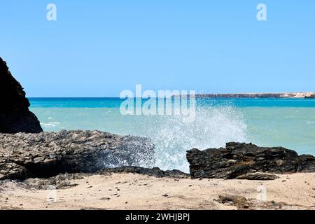 Der Atlantik in Jandia mit klarem Himmel und Bergen im Rücken und Wellen, die am Ufer brechen Stockfoto