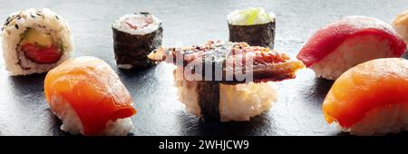 Sushi auf einem schwarzen Schieferplatten-Panorama. Nigiri mit Aal, Lachs und Thunfisch usw. Stockfoto